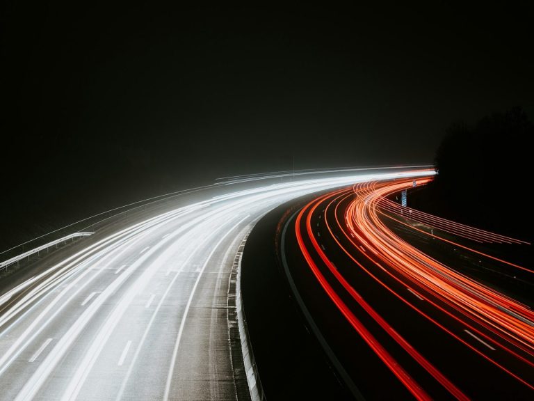 Lichtspuren von Fahrzeugen auf einer dunklen Straße bei Nacht.