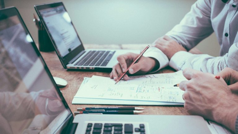 Strategic Consulting Zwei Personen arbeiten an Laptops und notieren etwas auf einem Blatt Papier.