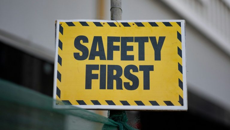 Functional Safety Gelbes Schild mit schwarzem Text "SAFETY FIRST" und Warnmuster.